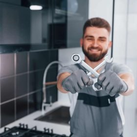 young-professional-plumber-in-grey-uniform-standing-on-the-kitchen-2.jpg